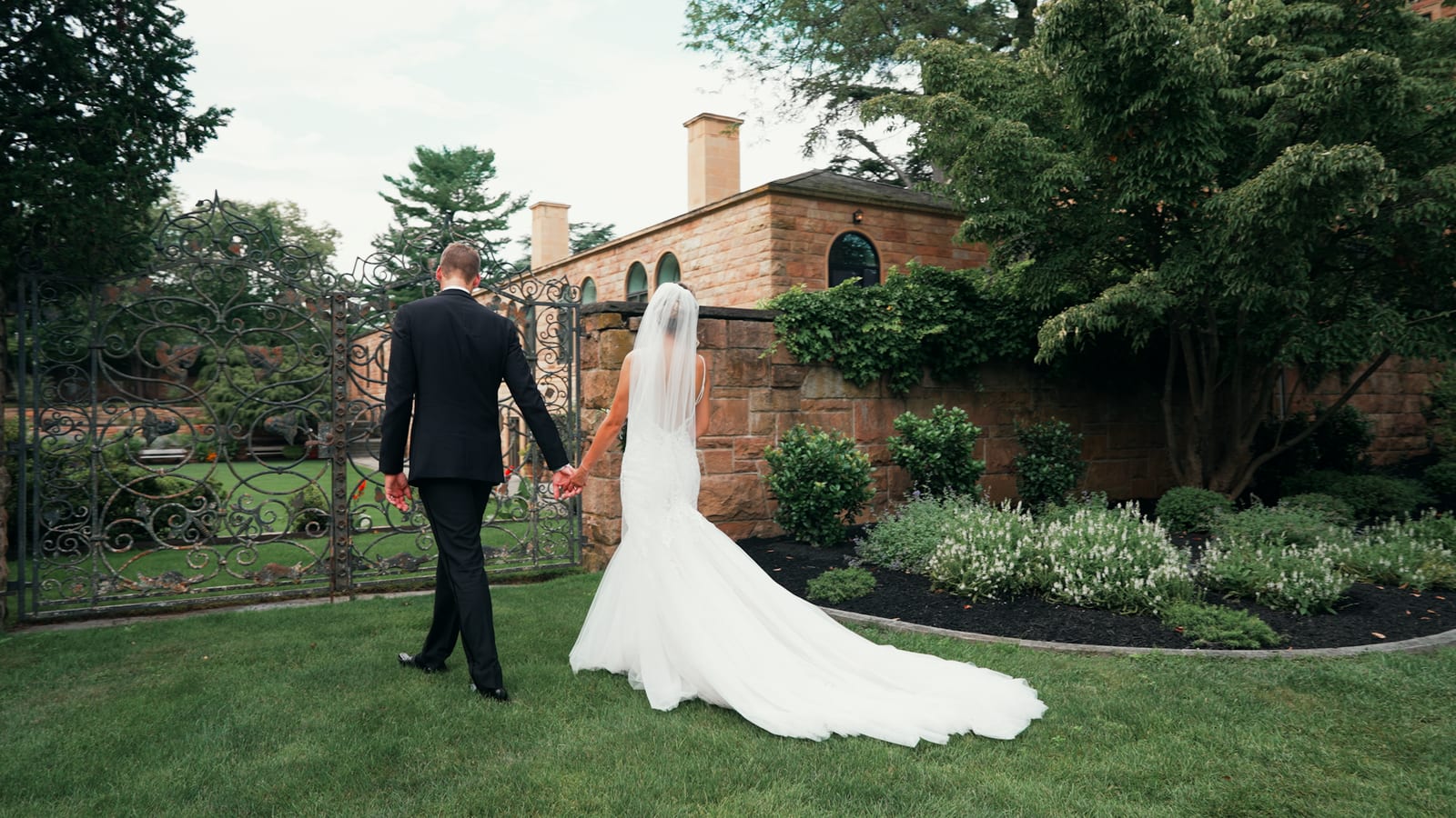 Jasna Polana Wedding Videography Karol and Victoria walking hand in hand through the garden courtyard gate